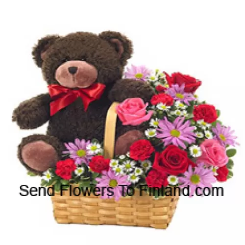Una hermosa canasta compuesta por rosas rojas y rosadas, claveles rojos y otras flores surtidas de color morado junto con un lindo oso de peluche de 14 pulgadas de altura